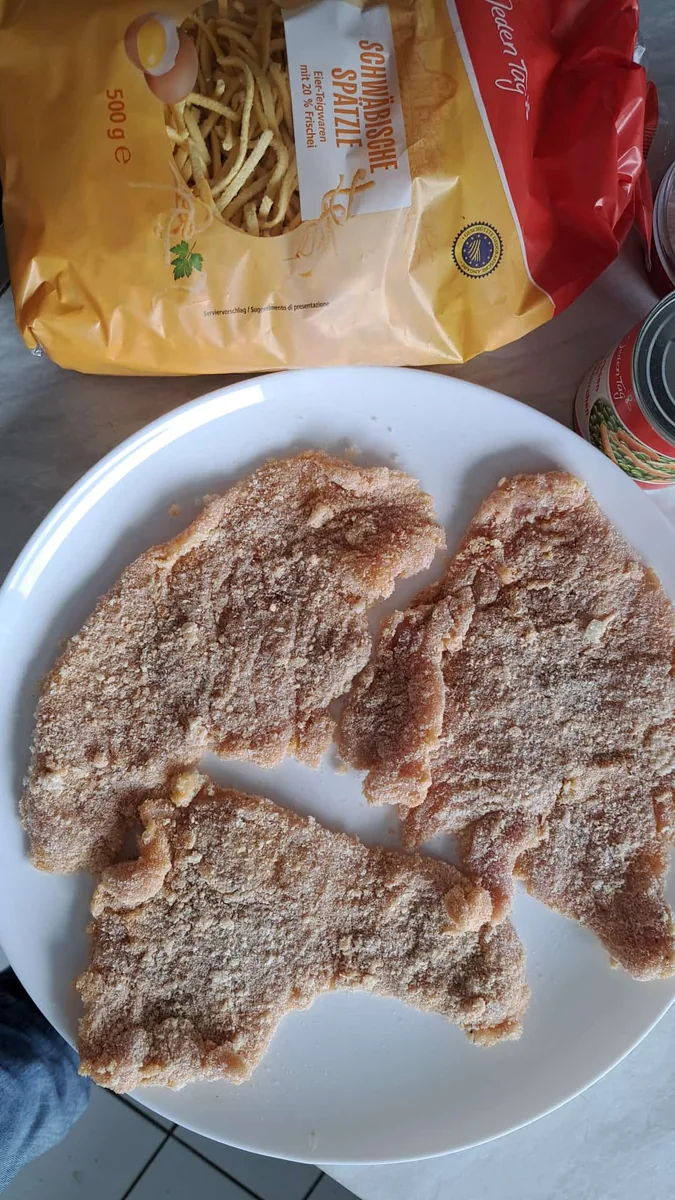 Panierte Schnitzel vor dem Braten auf einem weißen Teller